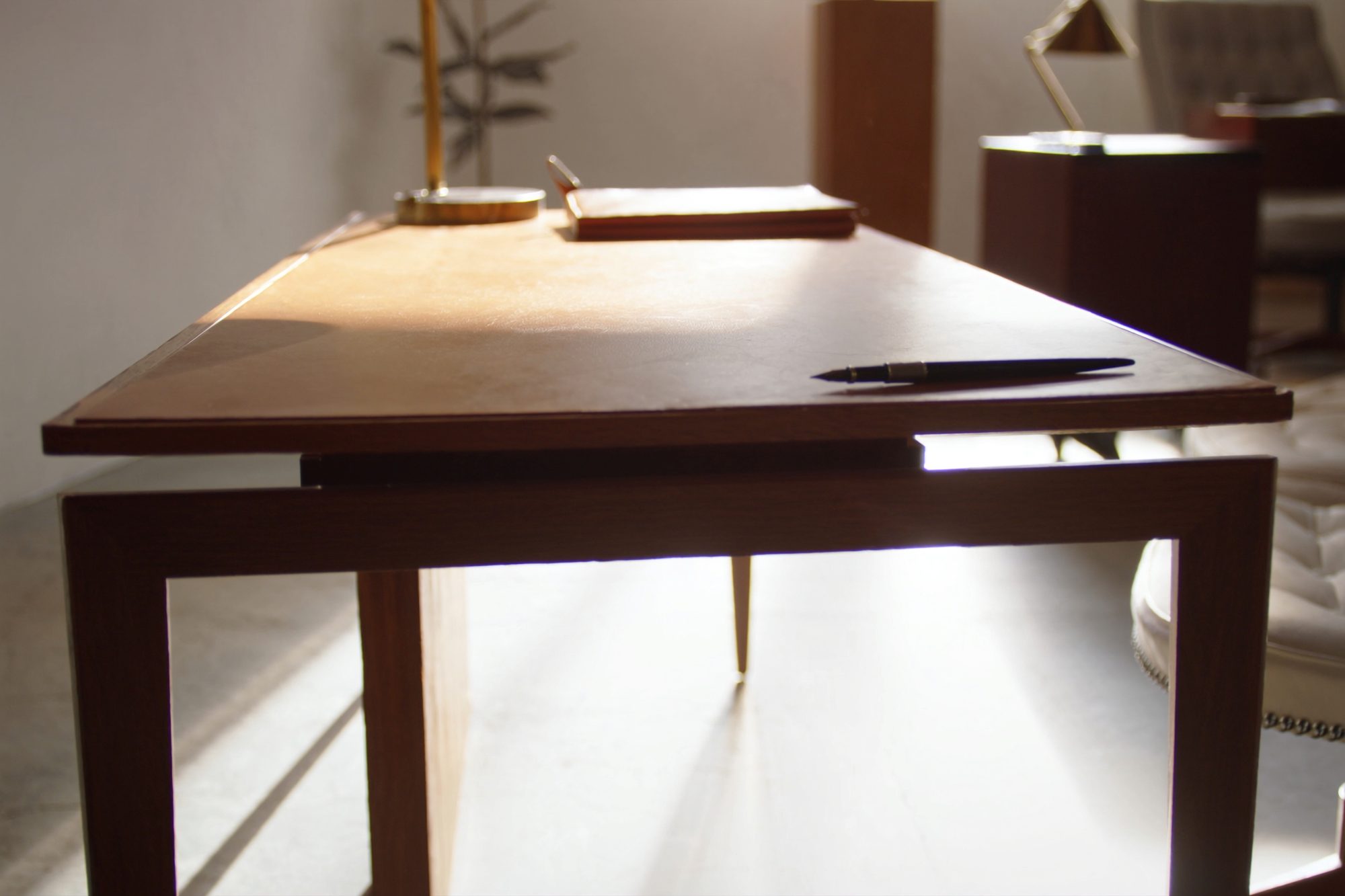 Detail of a walnut executive desk surface with a leather pad and brass lamp