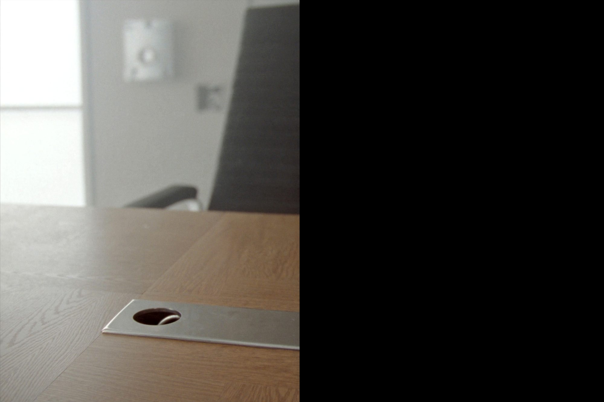 Detail of an oak conference table edge with a leather chair and a metal grommet