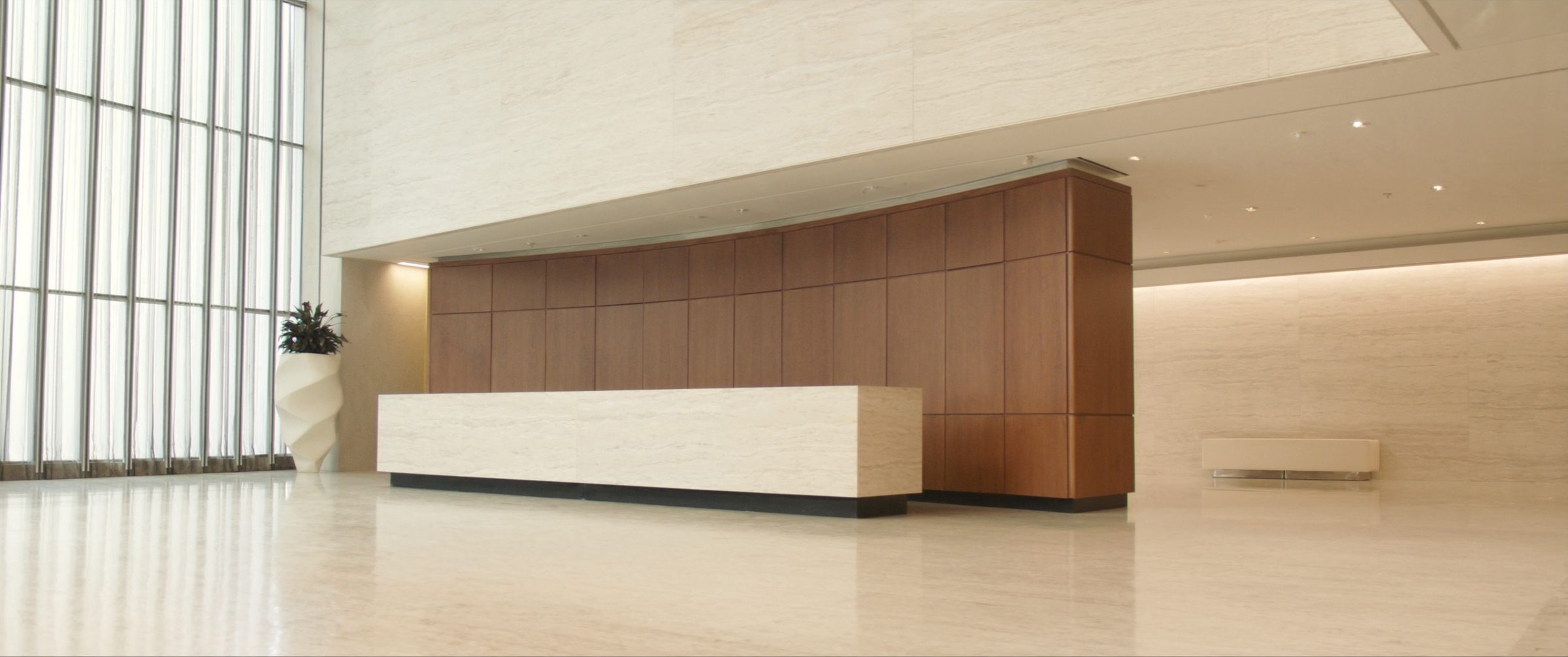 Corporate reception hall with a long travertine desk and warm walnut panelling