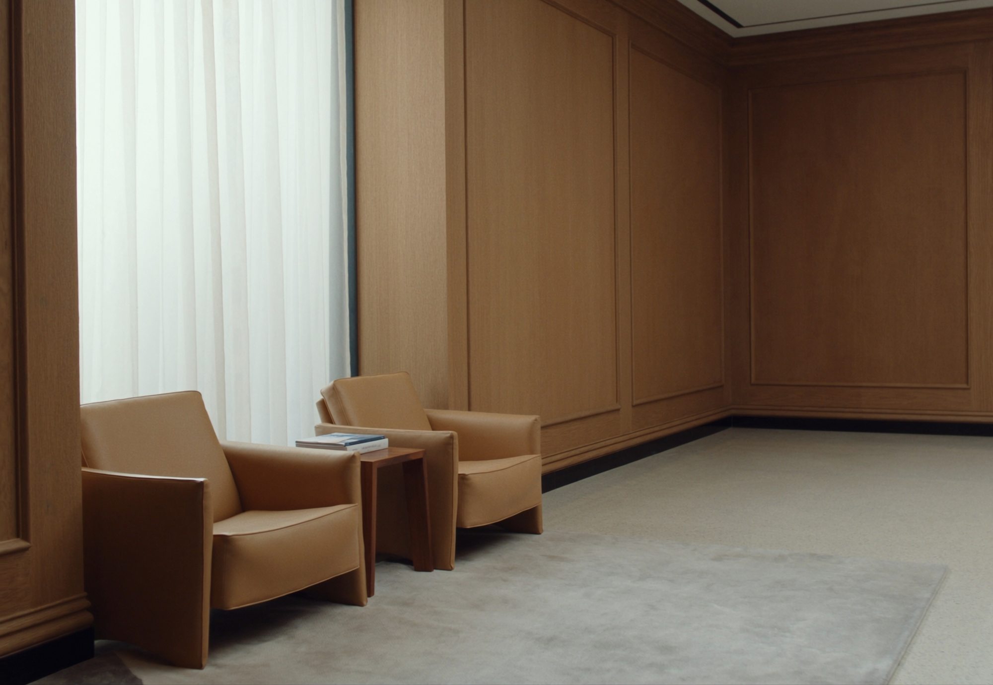 Reception waiting area with two tan leather lounge chairs and a walnut side table
